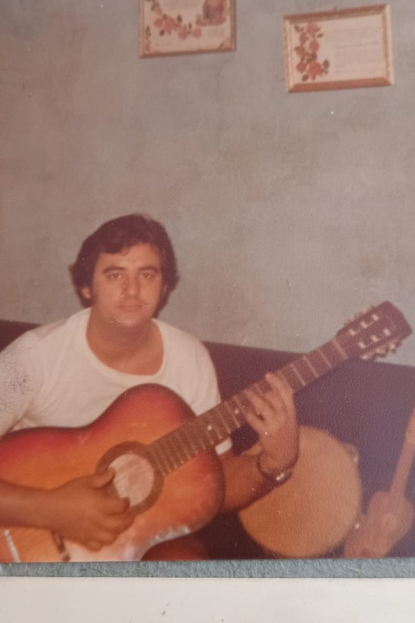 Fotografia antiga de um homem de camiseta branca tocando violão