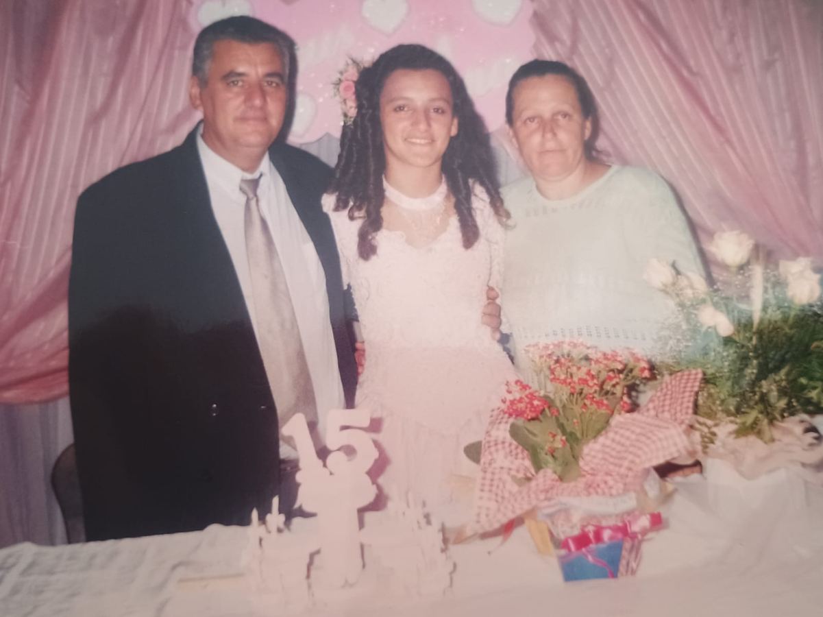 Fotografia antiga de um homem, uma menina de vestido rosa e uma mulher diante de um bolo