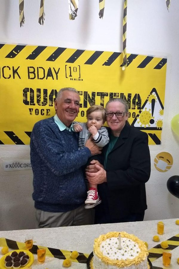 Um senhor segurando um bebê ao lado de uma mulher, em uma festa de aniversário