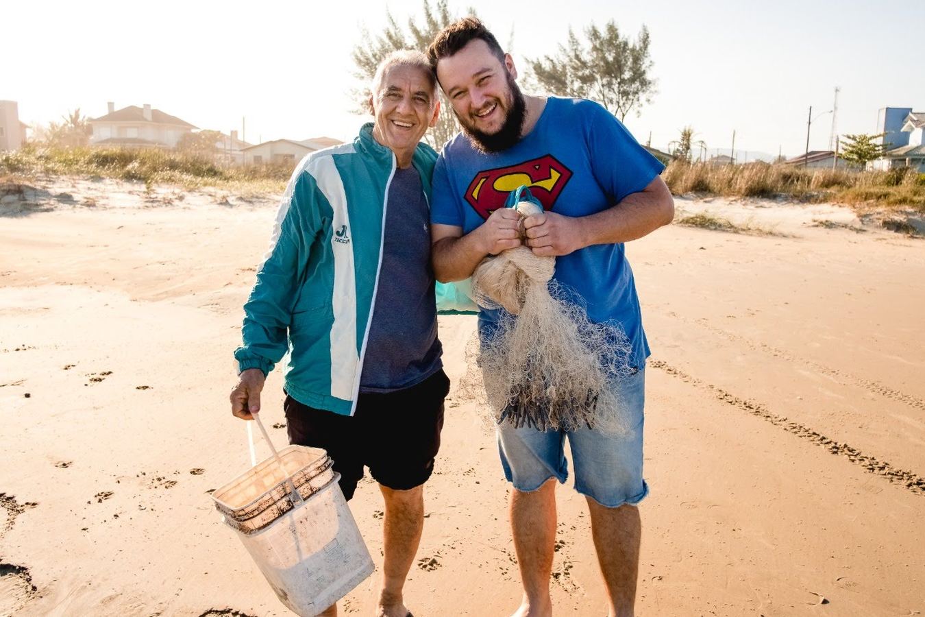 Um senhor e um rapaz numa praia, segurando uma rede de pesca