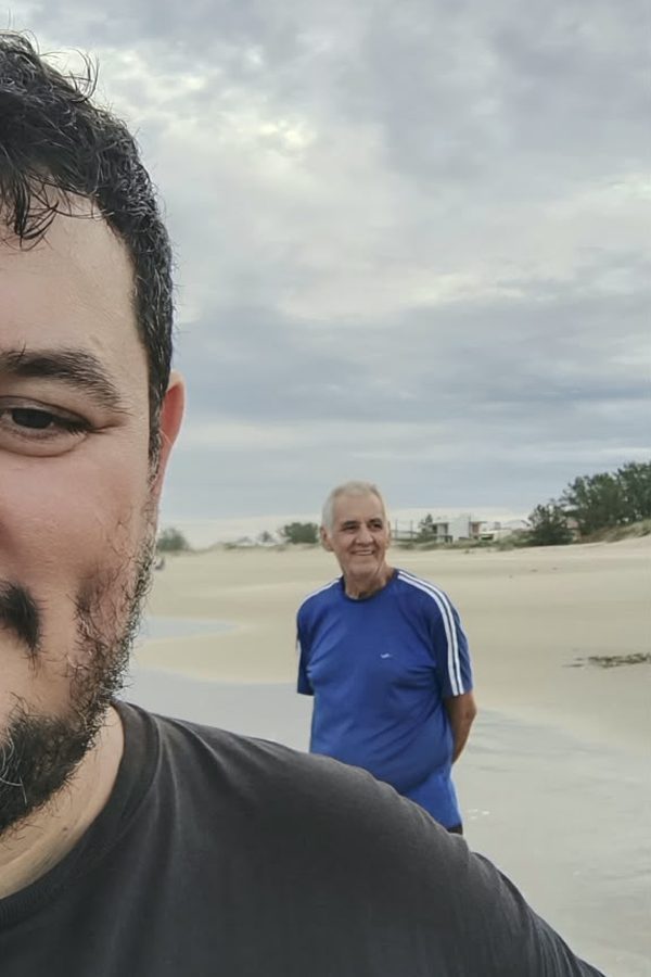 Selfie de um rapaz com Sinval ao fundo, numa praia