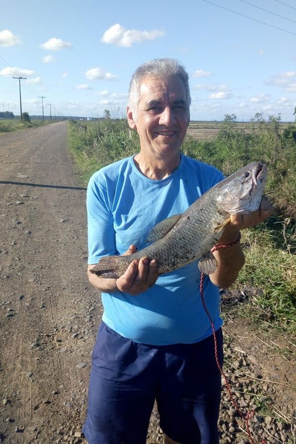 Sinval sorrindo, segurando um peixe numa estrada de terra