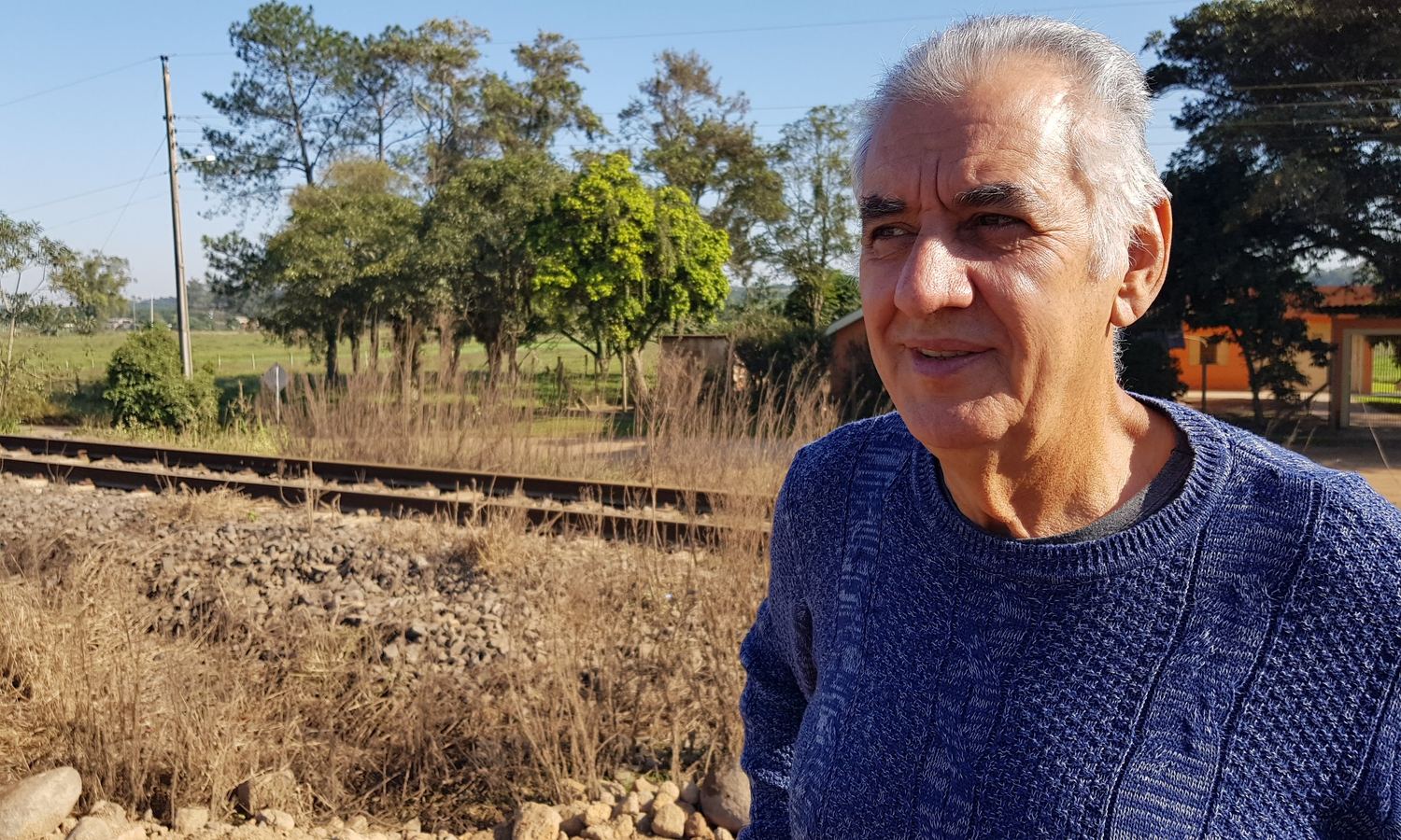 Sinval sorrindo, com a linha do trem ao fundo