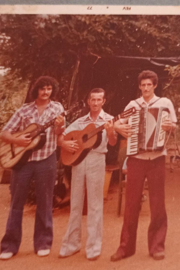 Três homens tocando instrumentos ao ar livre, em fotografia antiga