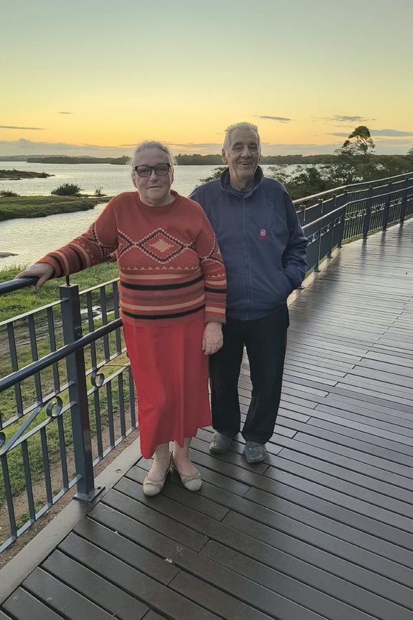 Sinval e uma mulher de pé num deque ao entardecer