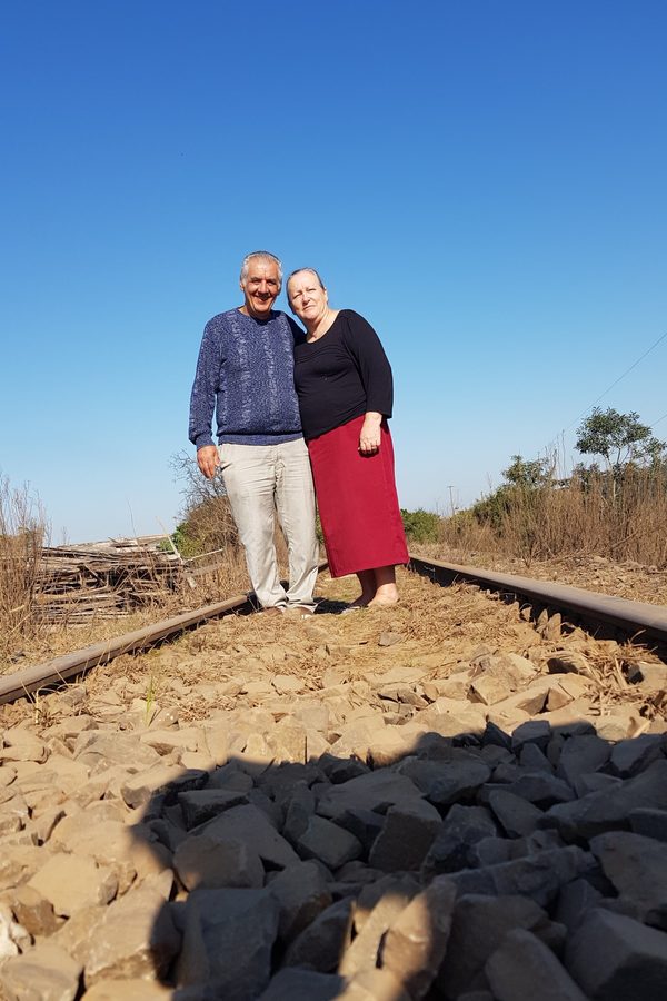 Casal abraçado sobre os trilhos de um trem, sob céu azul