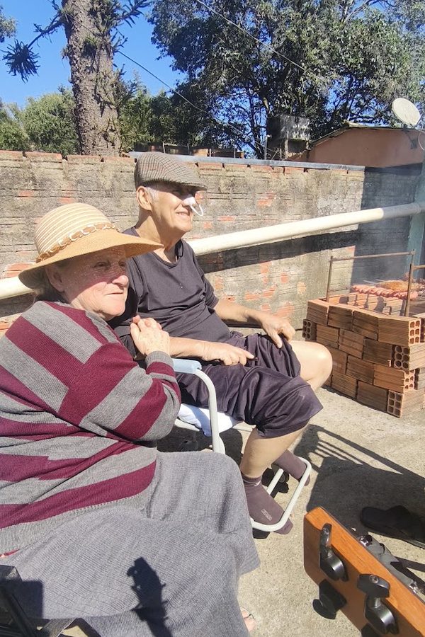 Casal de idosos sentados ao sol, vistos de costas