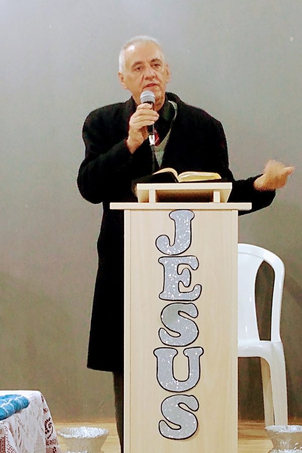 Sinval com o microfone junto a um púlpito com a palavra Jesus