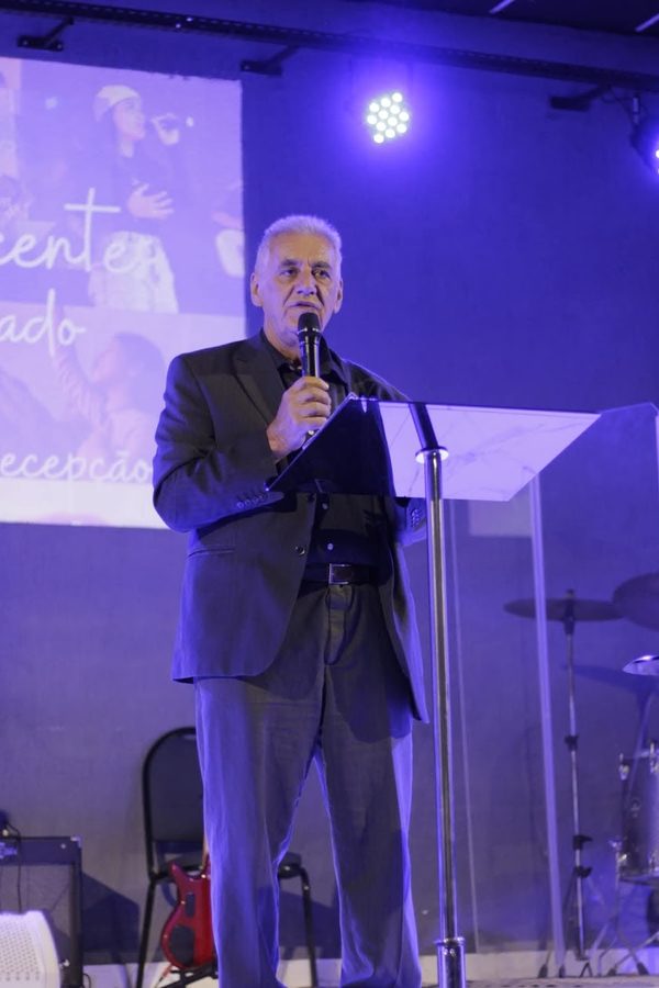 Sinval pregando com o microfone, em um palco iluminado