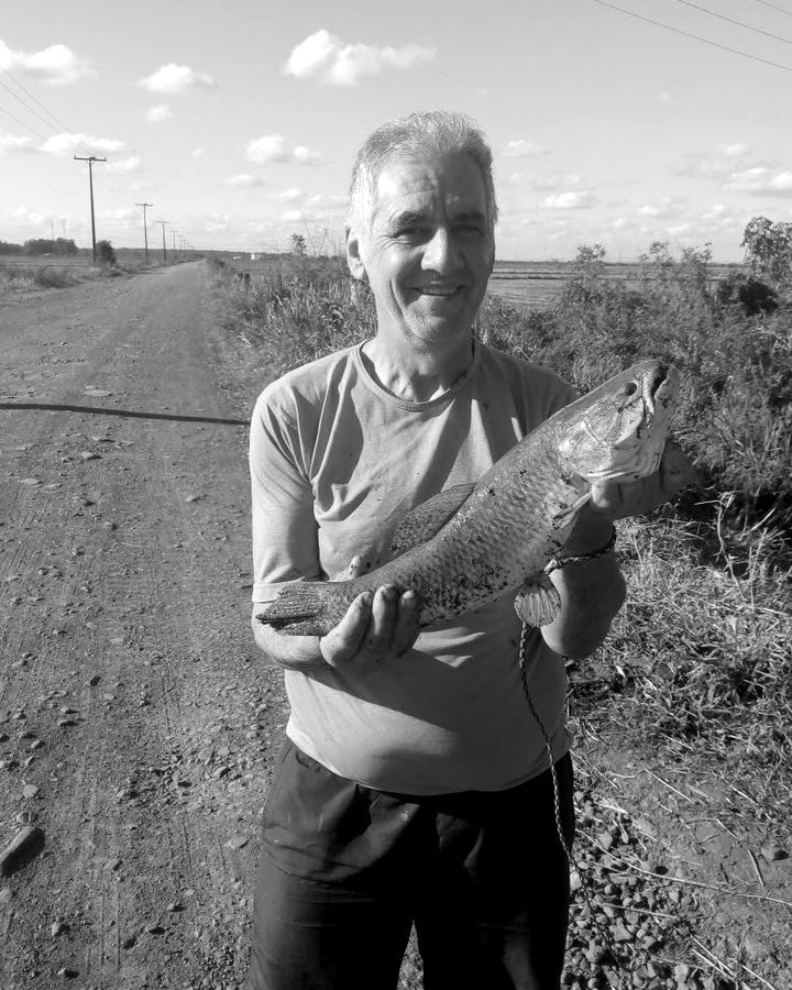Sinval sorrindo, segurando um peixe numa estrada de terra